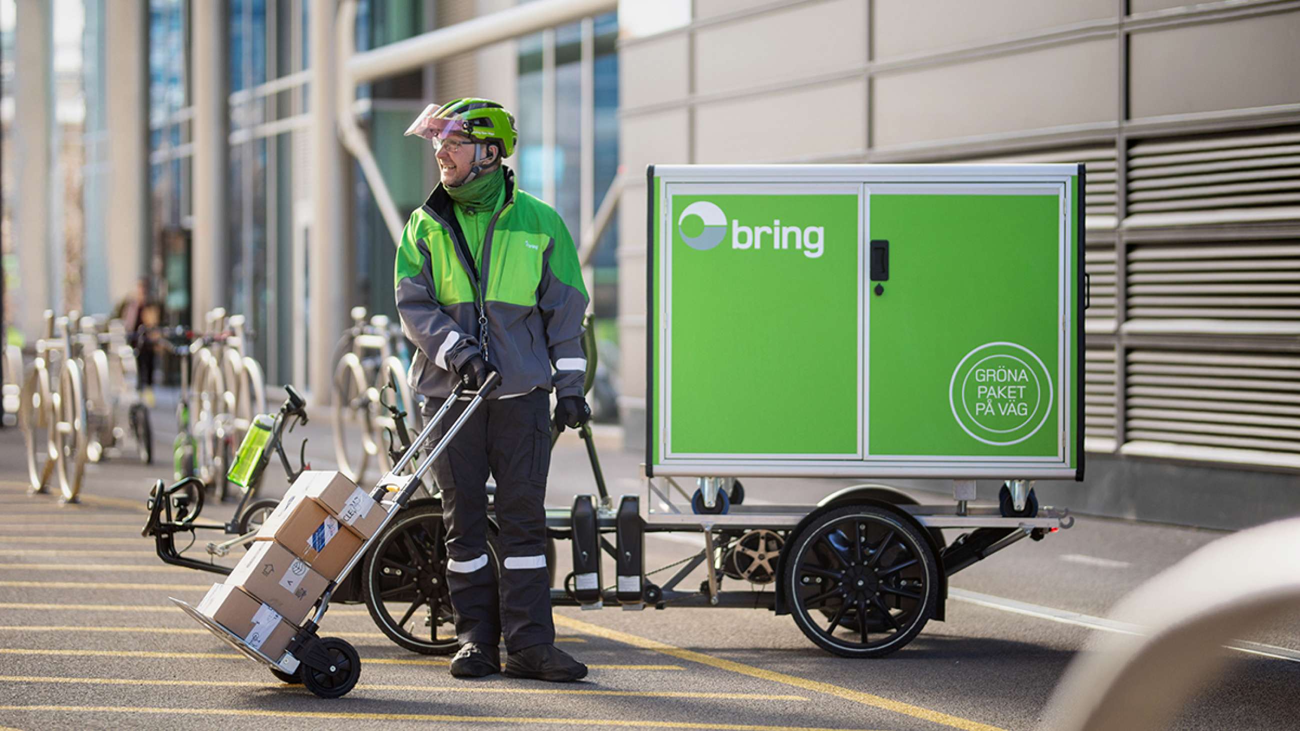 A Bring driver standing with a cart with parcels next to an electric bike