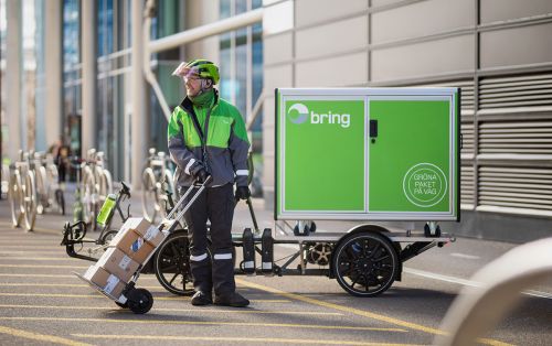 A Bring driver standing with a cart with parcels next to an electric bike